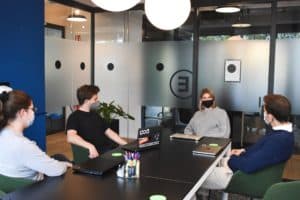 Two people sit at conference table with masks on