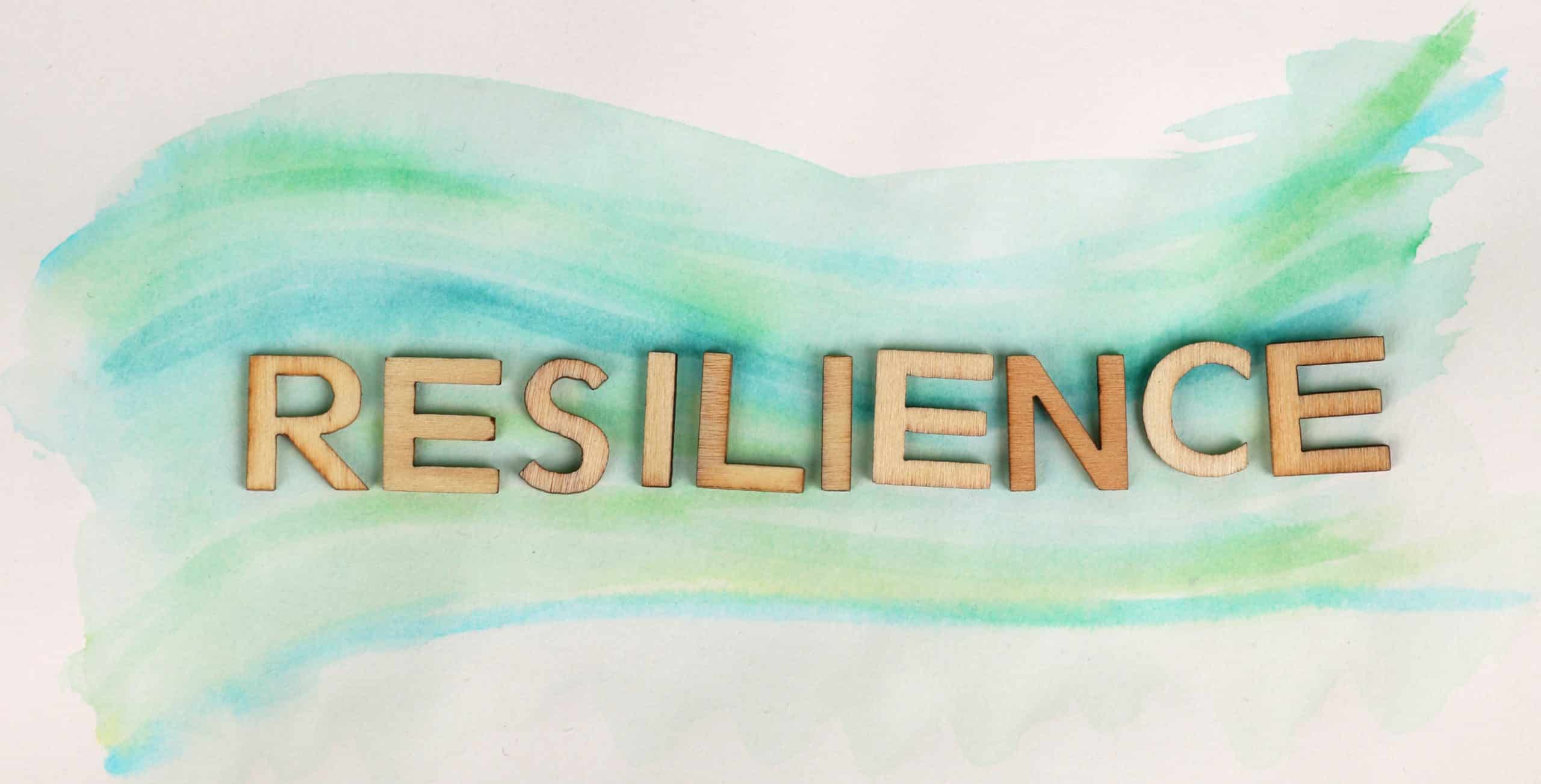 Wooden block letters spell "resilience" laying on a painted watercolor wave of blue and green