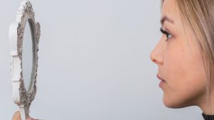 A woman looking at herself in a hand-held mirror.